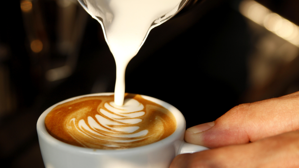 Milk being poured into a latte in a ceramic cup