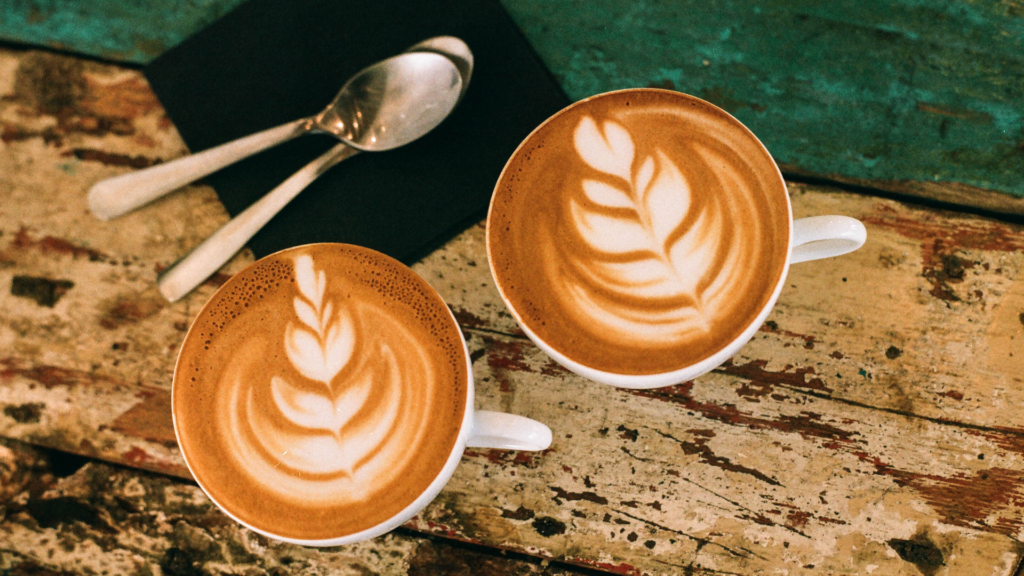 Two lattes in ceramic cups with latte art and spoons beside them