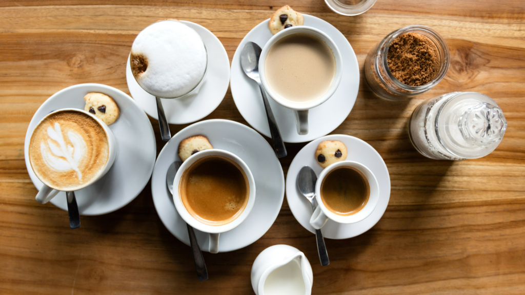 A variety of types of coffee on a wooden table showing different strengths with coffee and sugar on bowls beside