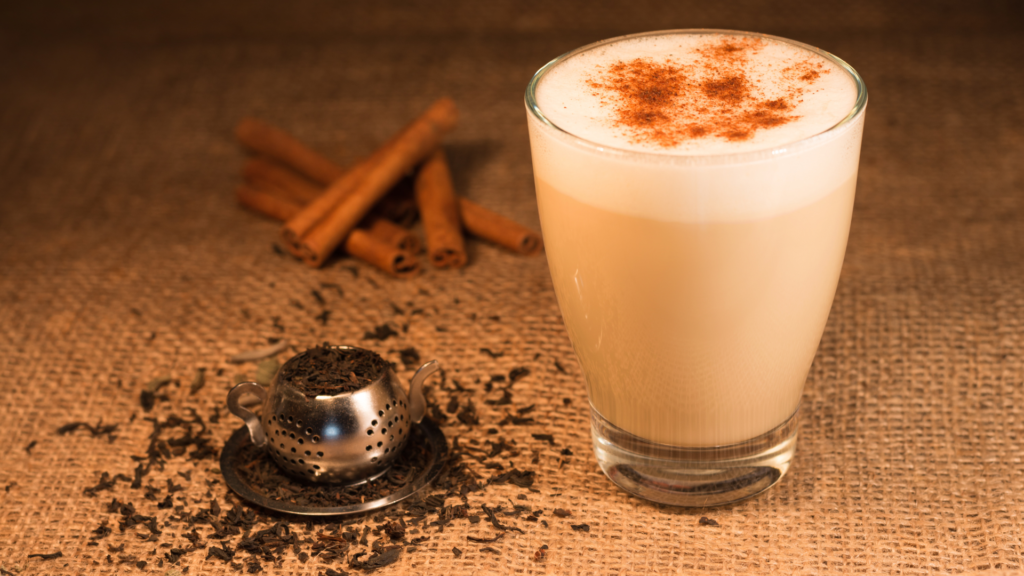 A large chai latte with spices around it in a glass cup
