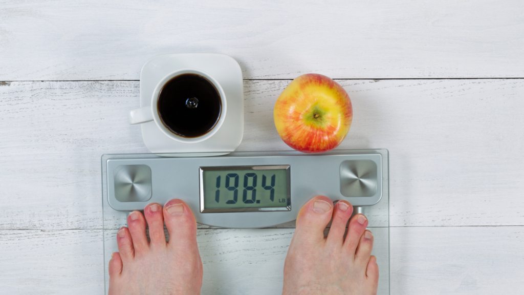 Feet on a weight scale with coffee and an apple in front of it